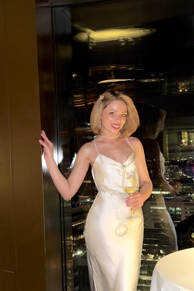 Laine in a white satin dress with a glass of wine