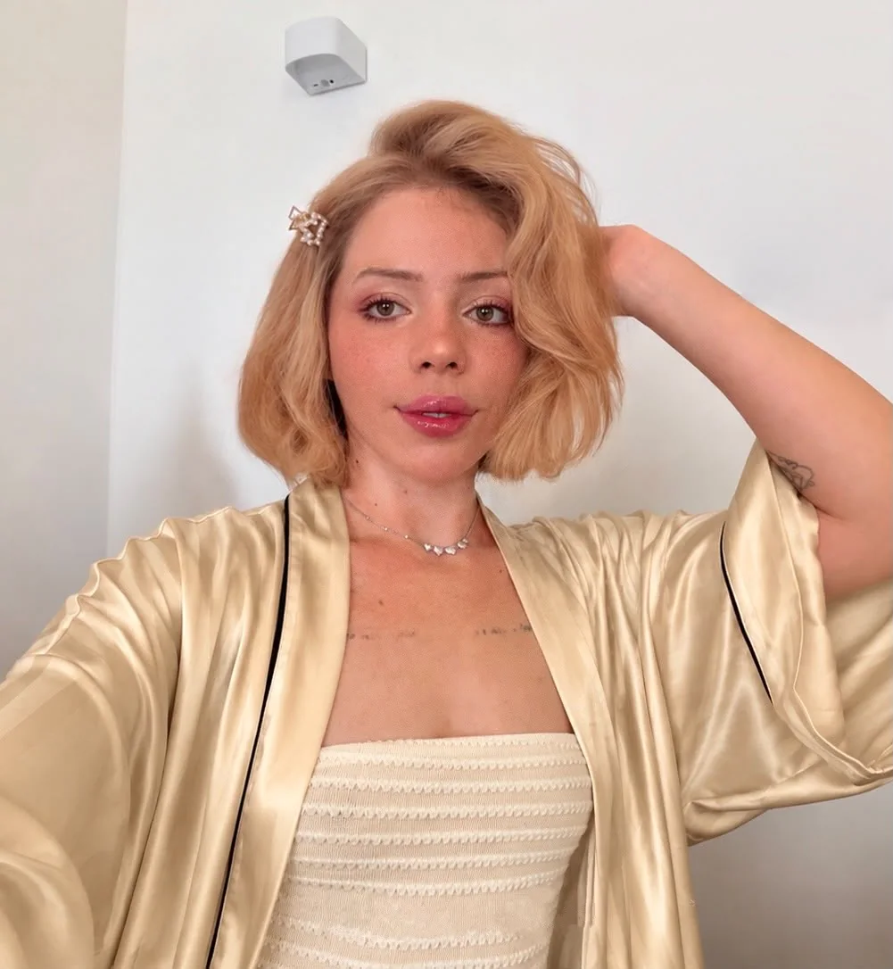 Laine in a gold satin robe, smiling, one hand in her hair